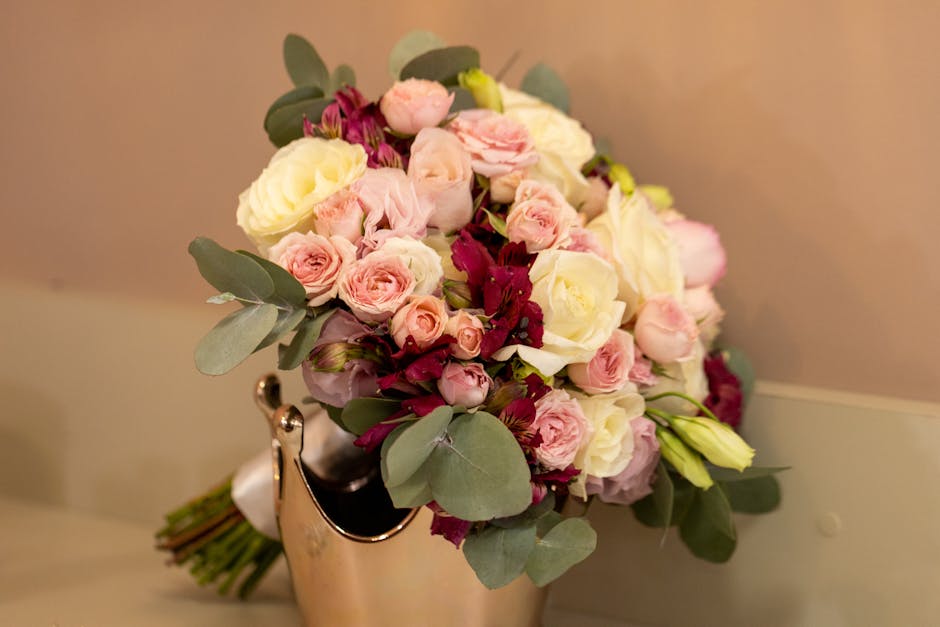 A bouquet of fresh flowers featuring pale pink roses, white roses, and deep red blooms, accented with green eucalyptus leaves. The arrangement is gathered in a cascading style, with some flowers and f