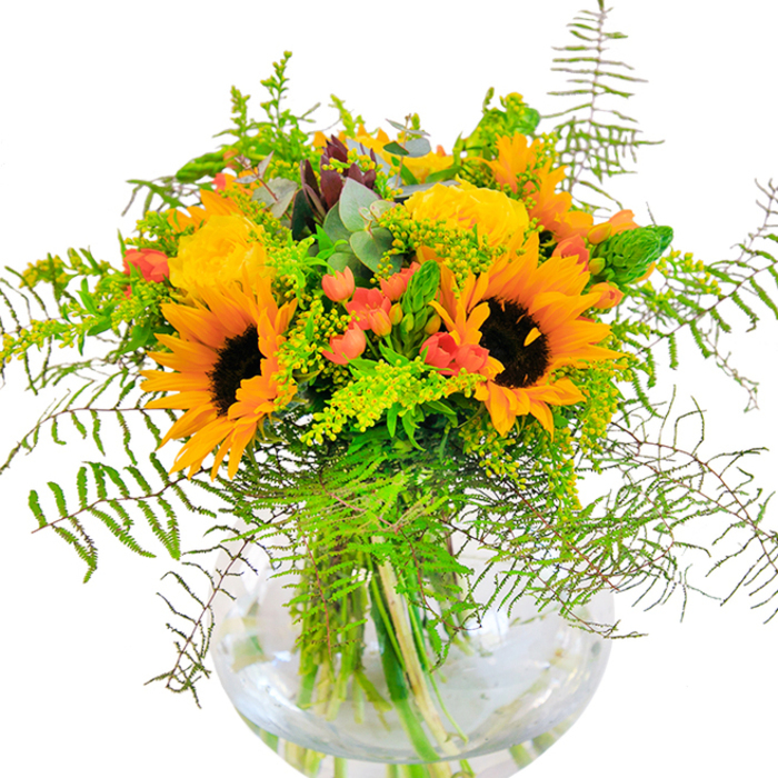 Sunlight seems to pour from this arrangement, where vibrant yellow roses and exuberant sunflowers come together in a joyful display reminiscent of Bromley's summer festivals. Each sunflower is rimmed with bold yellow petals and accented by dark, textured centers, exuding a sense of positivity. The roses' tightly coiled petals bring a soft elegance, their notes of gold and cream harmonizing with the composition. Interspersed throughout, clusters of ruby-red hypericum berries glossily catch the light, while verdant fern fronds and tassels of delicate, pale-green filler add richness and volume-evoking the abundant greenery of Kelsey Park. Muted eucalyptus leaves peek through, adding a refined touch and subtle freshness. All elements are arranged carefully inside a spherical, clear glass vase, which allows the crisscross of stems and clarity of water to anchor the vibrant top. One can imagine the gentle interplay of textures: the pillowy softness of the rose petals, the rustle of greenery, the cool solidity of glass. The bouquet is fragrant, understated, and lively-a fitting tribute for birthdays, new beginnings, or offering a bright welcome into a Bromley home, courtesy of Bromley Florist.